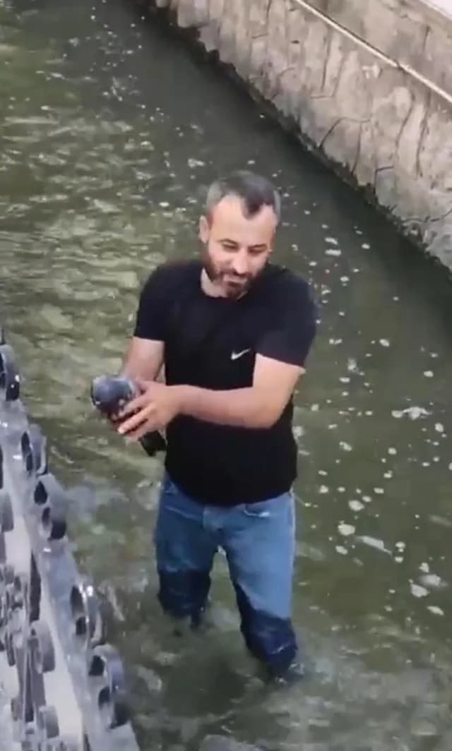 Su kanalının içinde duran, elinde kurtardığı güvercini tutan siyah tişörtlü bir erkek
