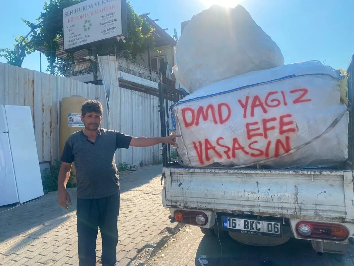 Kağıt toplayıcısı bir adam, kamyonet üzerindeki balyaya yazılı 'DMD Yağız Efe Yaşasın' yazısını işaret ediyor