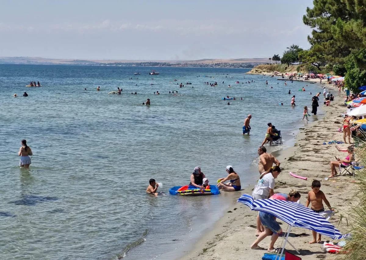 Kalabalık sahilde denize giren ve şezlonglarda dinlenen tatilciler
